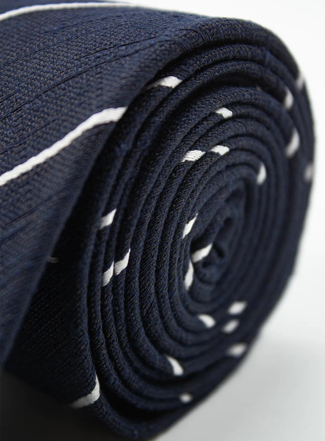 Roll of navy fabric with white stitching on a light gray background