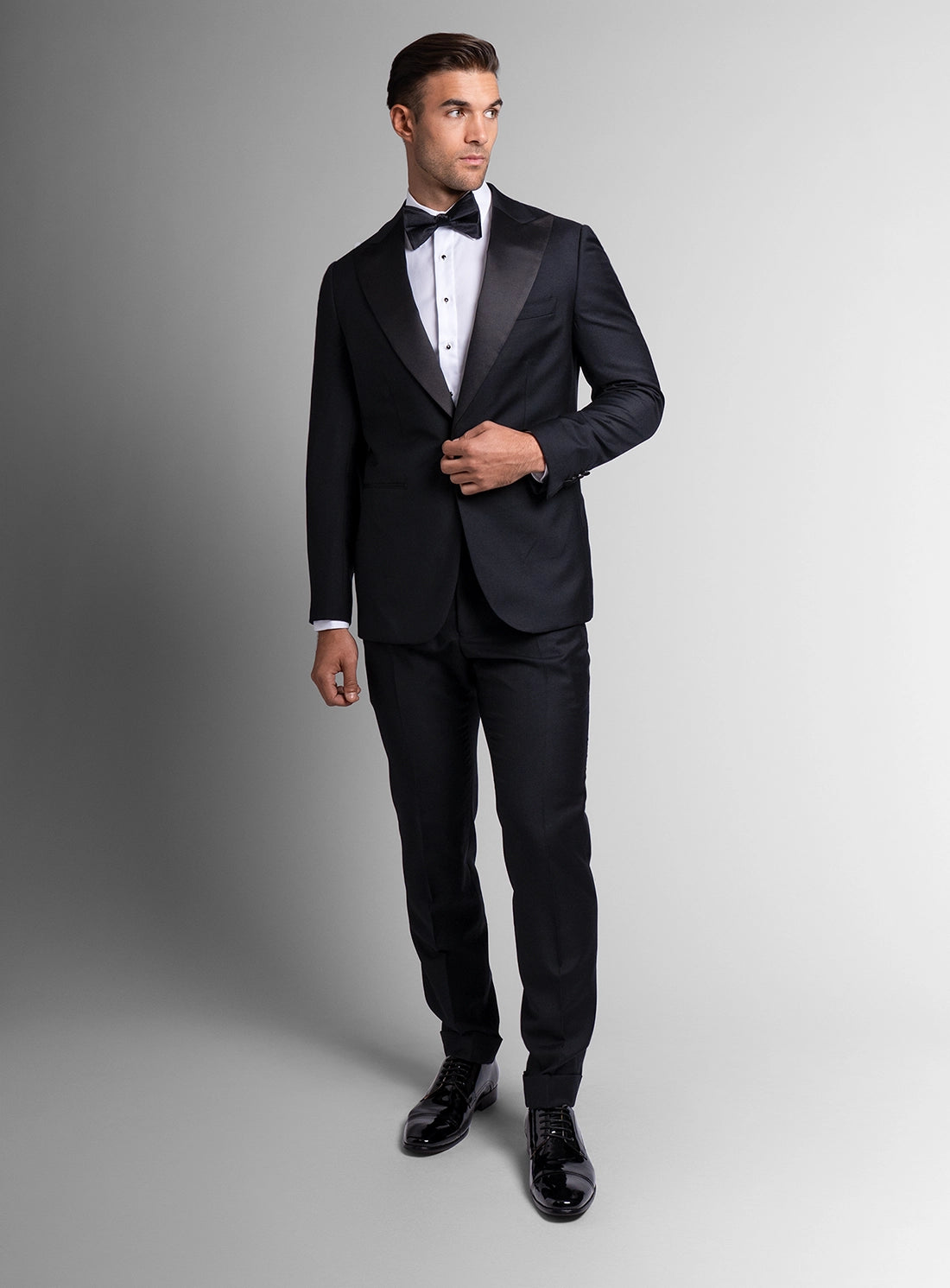 Man wearing a black tuxedo with a white shirt and black bow tie on a gray background