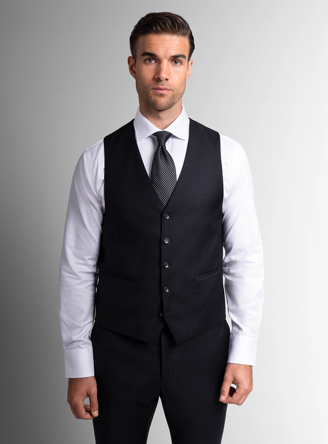 Man wearing a black vest over a white shirt with a gray tie against a gray background