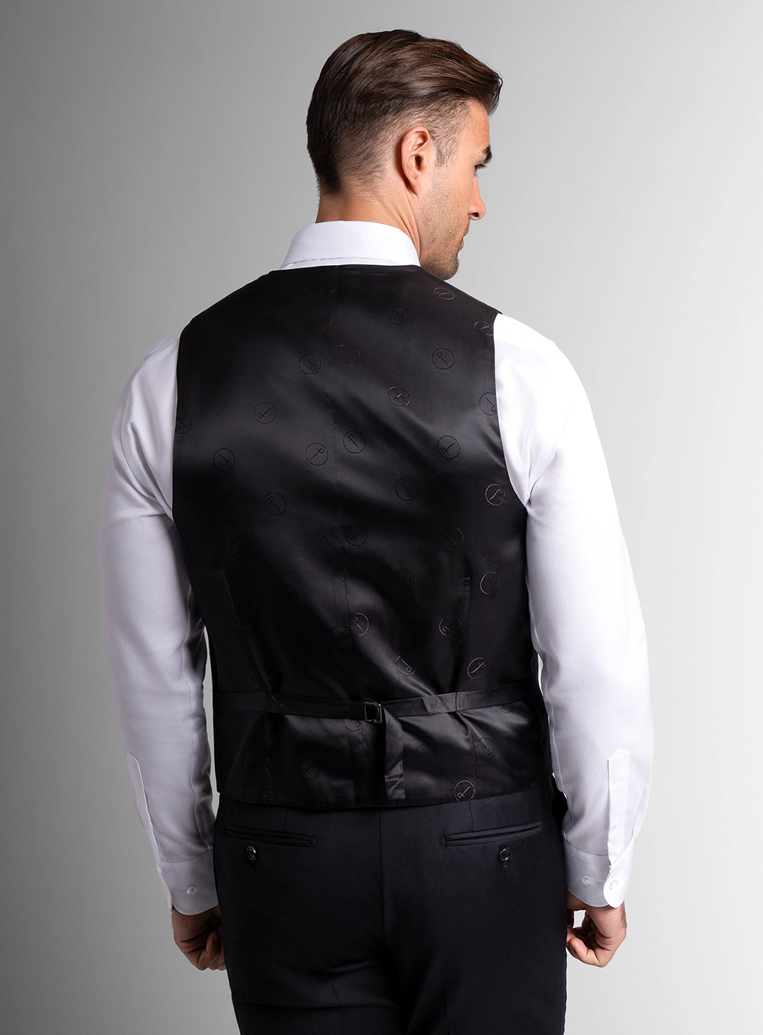 Man wearing a black vest over a white shirt on a gray background