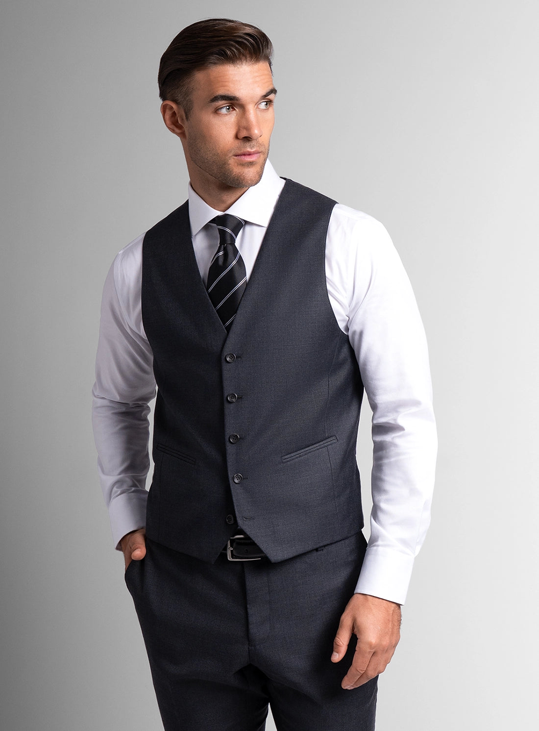 Man wearing a dark gray vest over a white shirt with a gray background