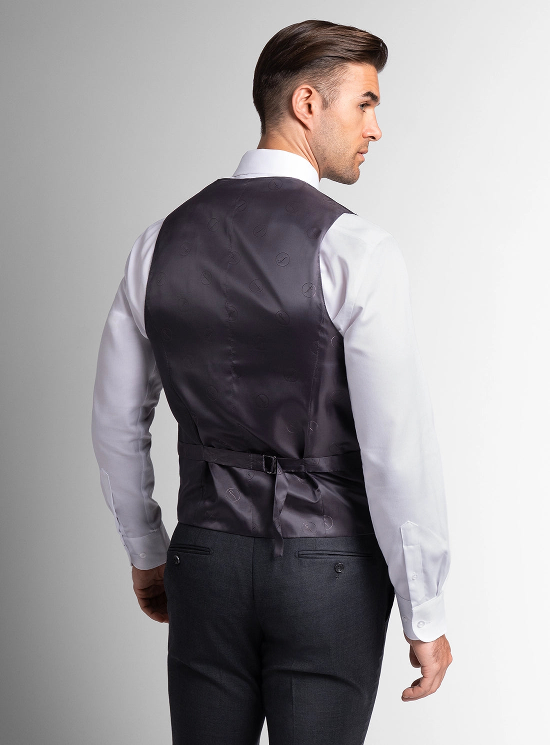 Man wearing a black vest over a white shirt on a gray background