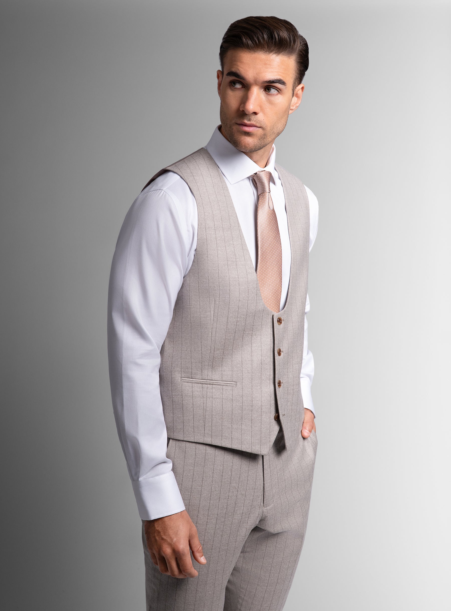 Man wearing a gray suit vest and pants with a white shirt and tie on a gray background