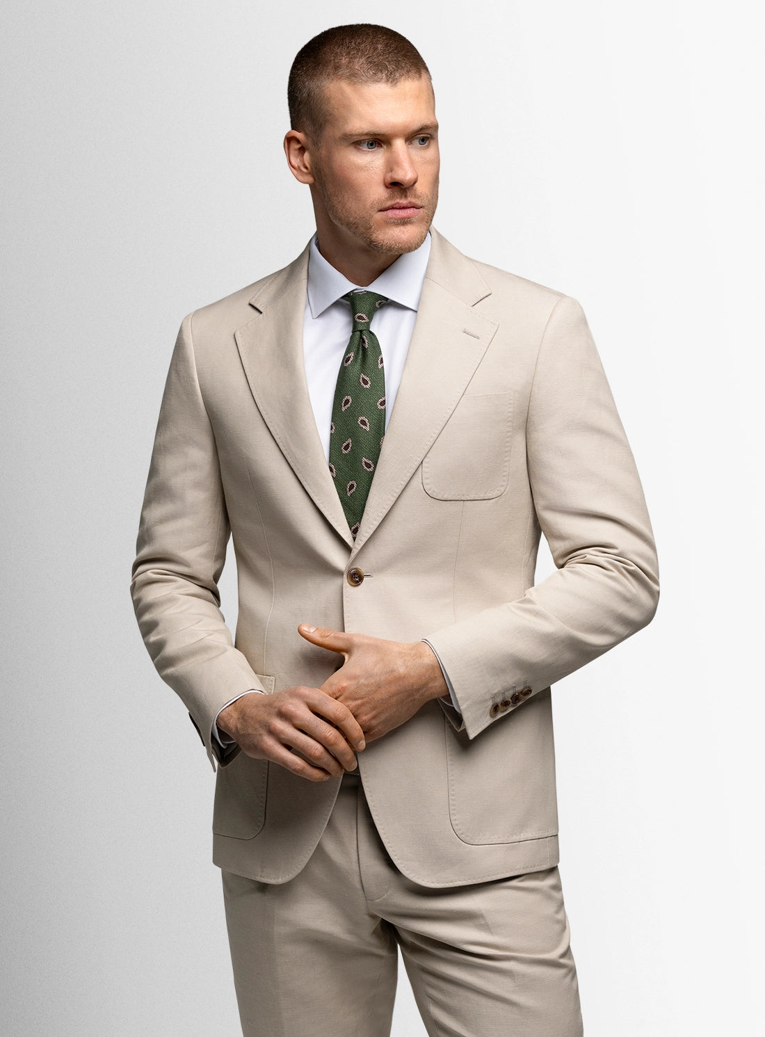 Man wearing a beige suit with a white shirt and green tie on a light gray background
