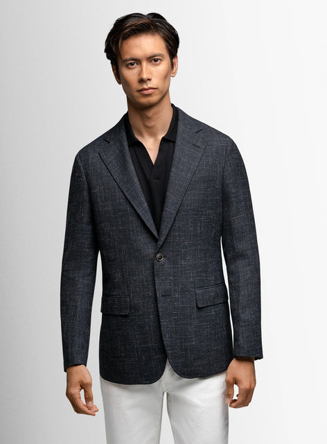Man wearing a dark blue blazer over a black shirt on a light gray background