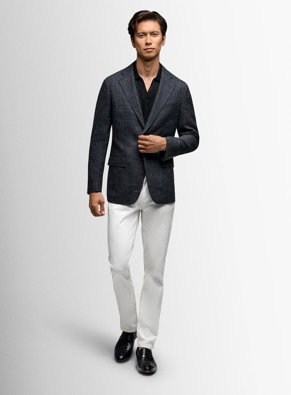 Man wearing a dark blazer, white shirt, and white pants on a light gray background