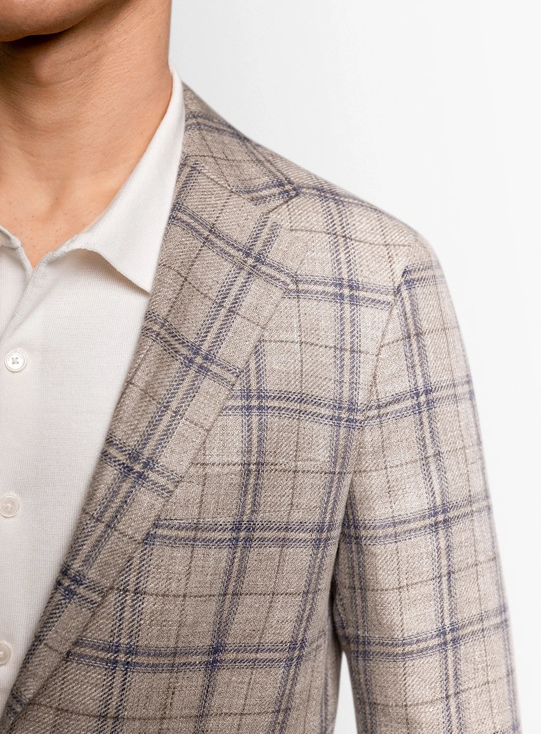 Close-up of a person wearing a beige checkered blazer over a white shirt.