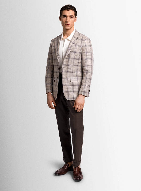 Man wearing a plaid blazer, white shirt, and dark trousers on a light gray background