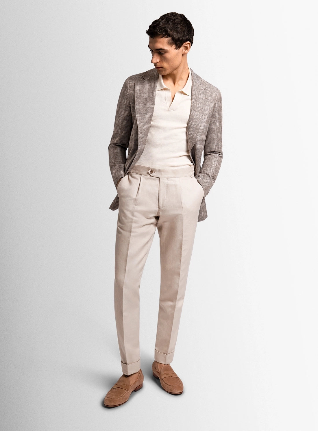 Man wearing a gray blazer, white shirt, beige pants, and brown shoes on a light gray background