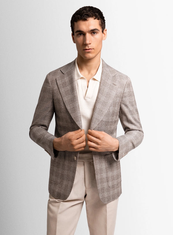 Man wearing a gray checkered blazer over a white shirt with beige pants on a light gray background