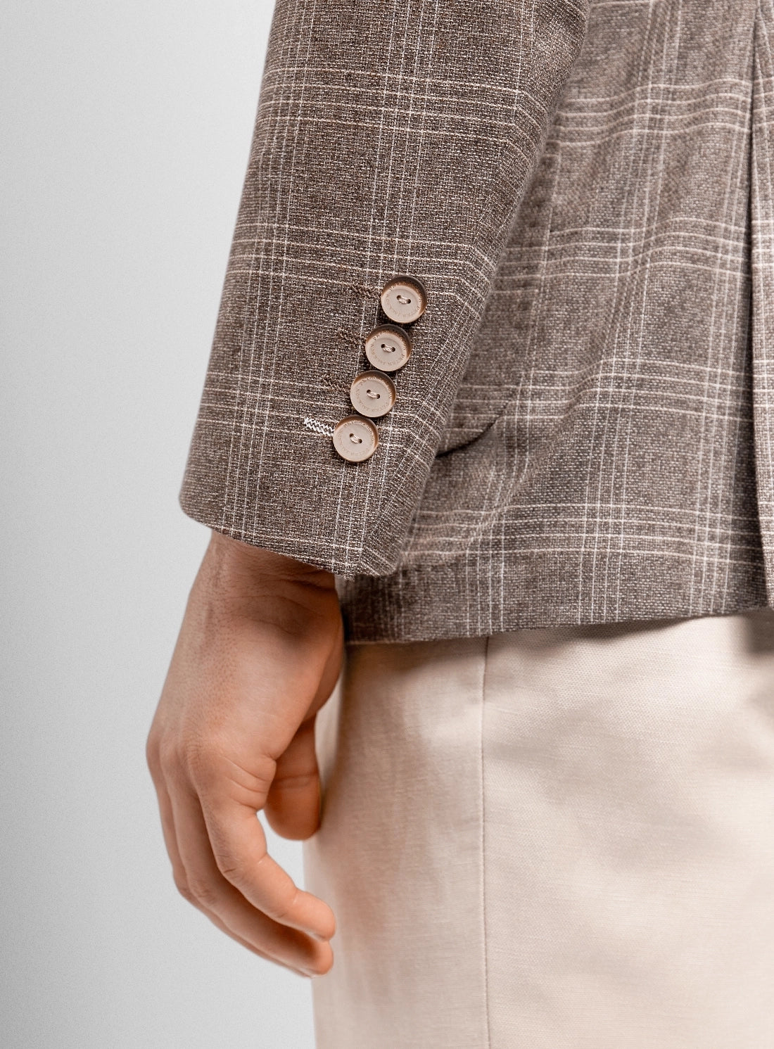 Close-up of a brown checkered jacket with three buttons on a light gray background