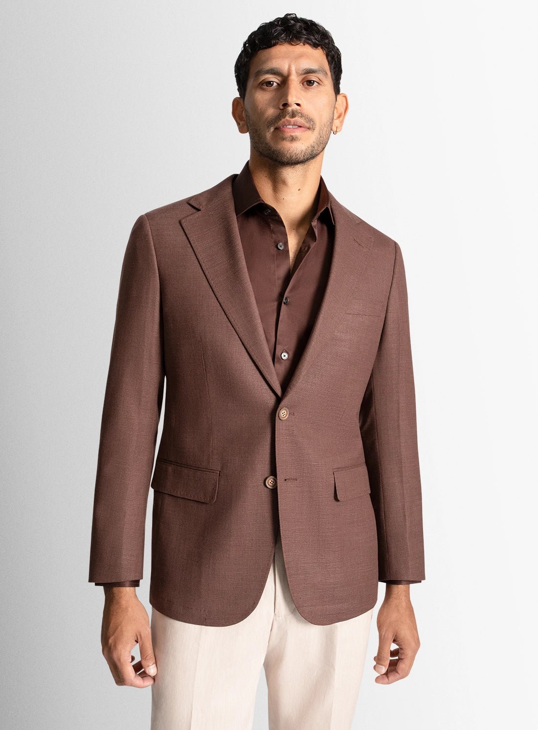 Man wearing a brown blazer over a shirt on a plain background