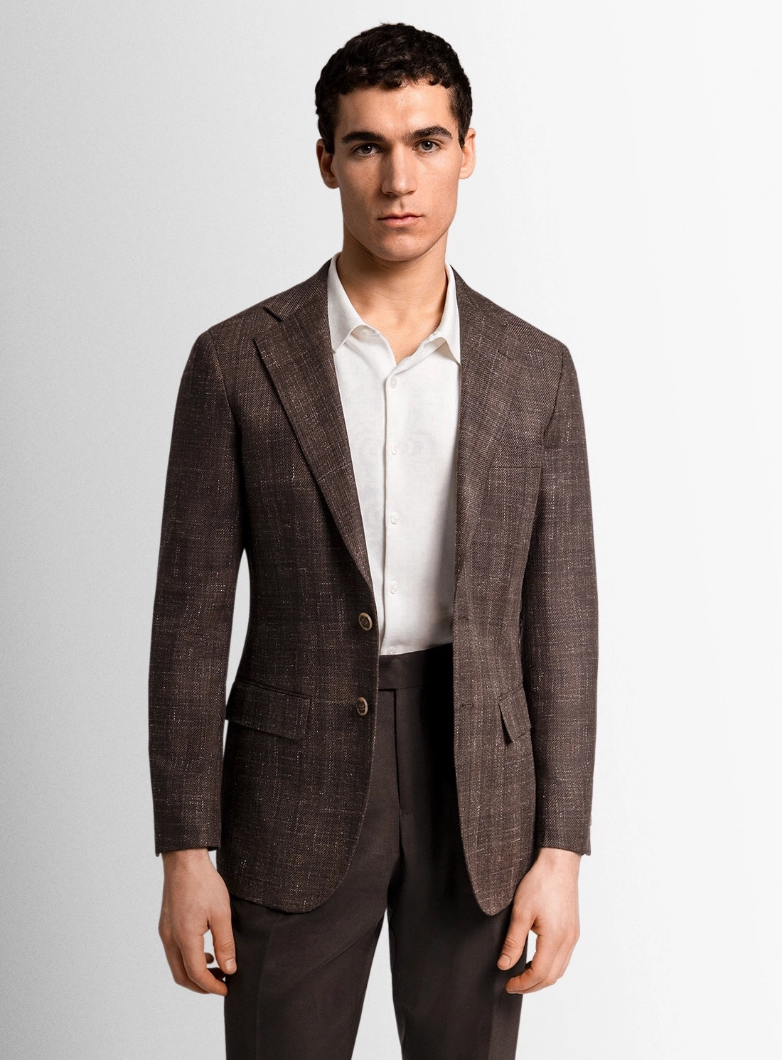 Man wearing a brown checkered blazer over a white shirt on a light gray background