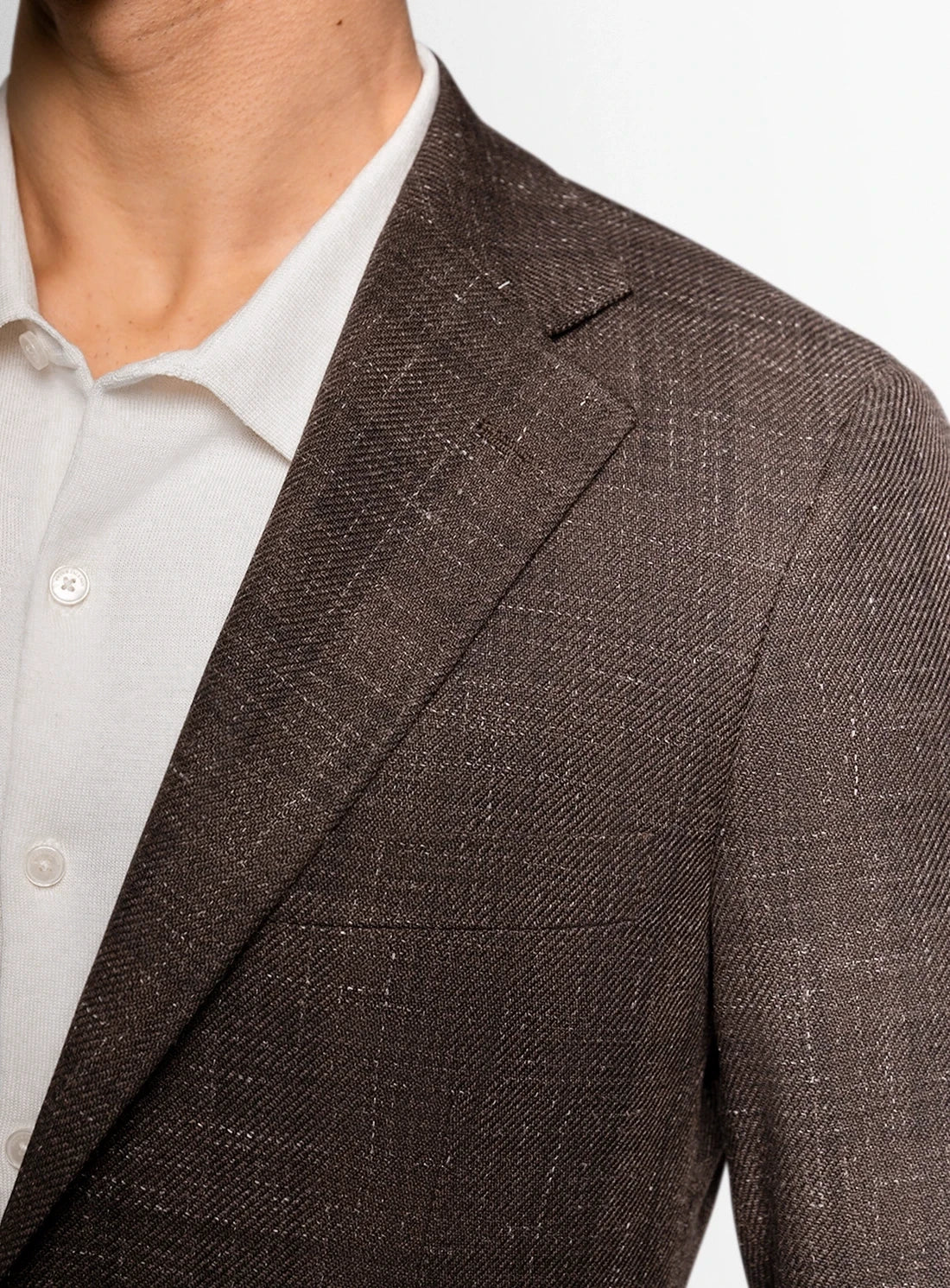 Close-up of a brown suit jacket worn over a white shirt on a light gray background