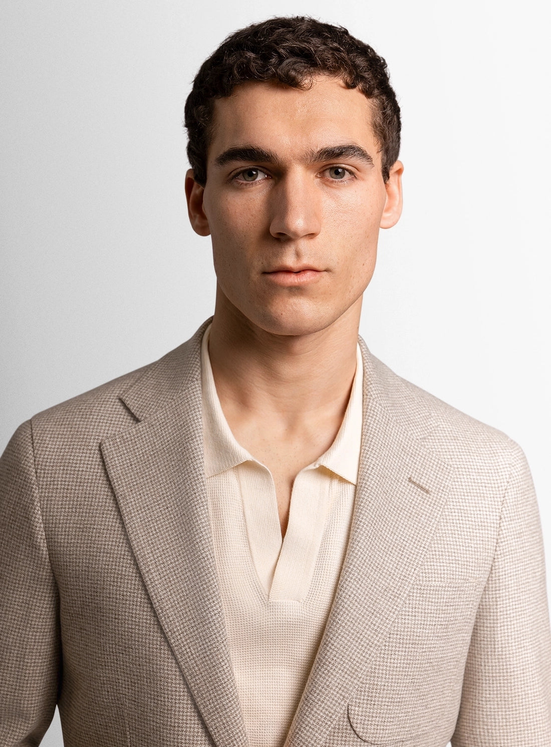 Man wearing a beige suit jacket over a white shirt against a plain background