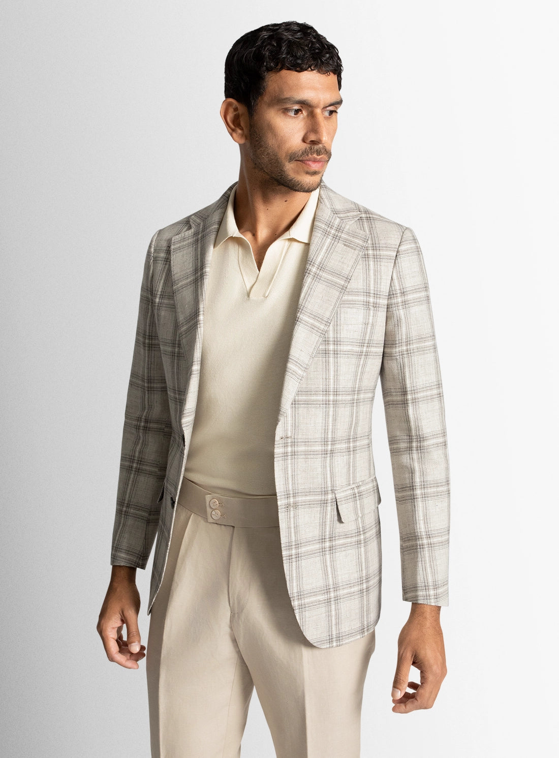 Man wearing a plaid blazer over a polo shirt and pants on a light gray background