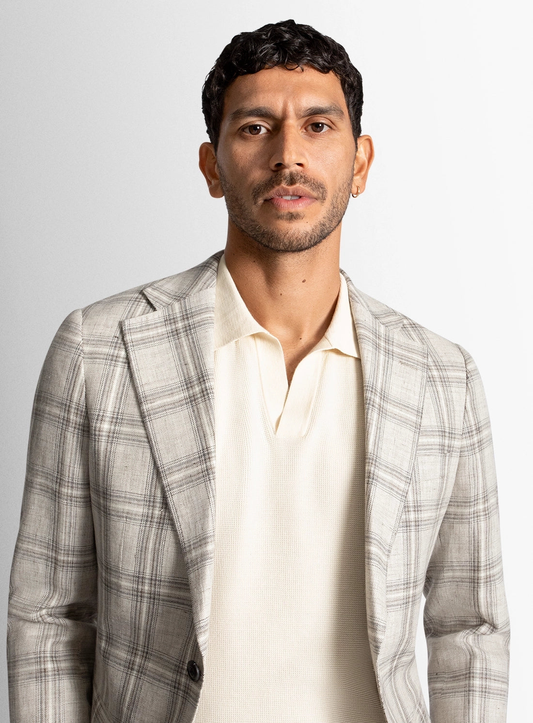 Man wearing a gray checkered blazer over a white shirt on a light gray background