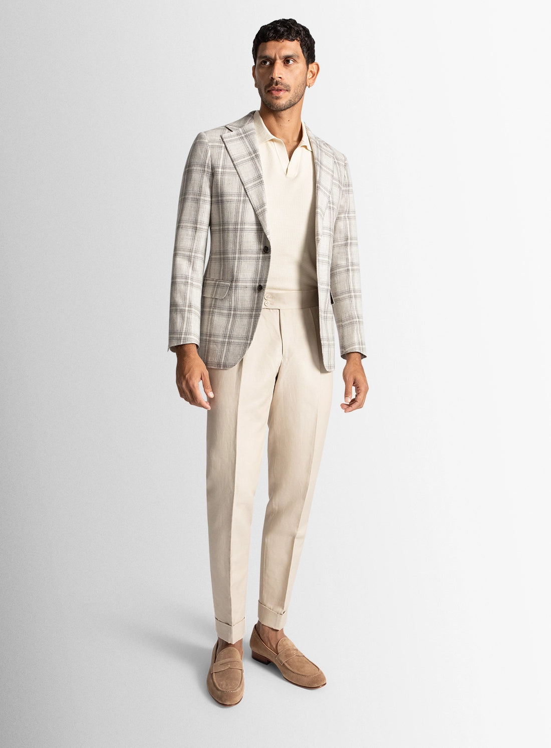 Man wearing a plaid blazer, white shirt, beige pants, and brown shoes on a light gray background