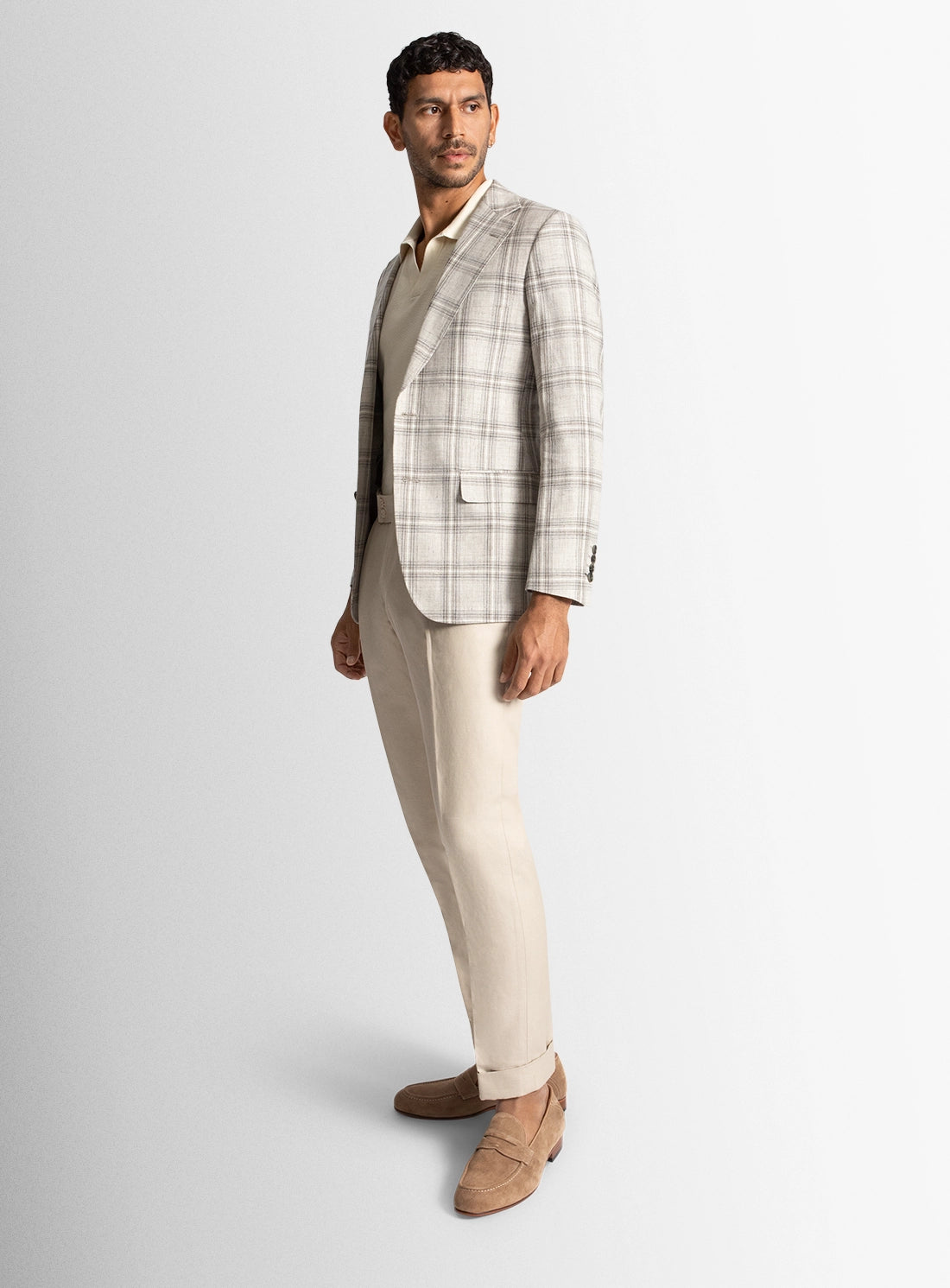 Man wearing a plaid blazer, beige shirt, and beige pants on a white background