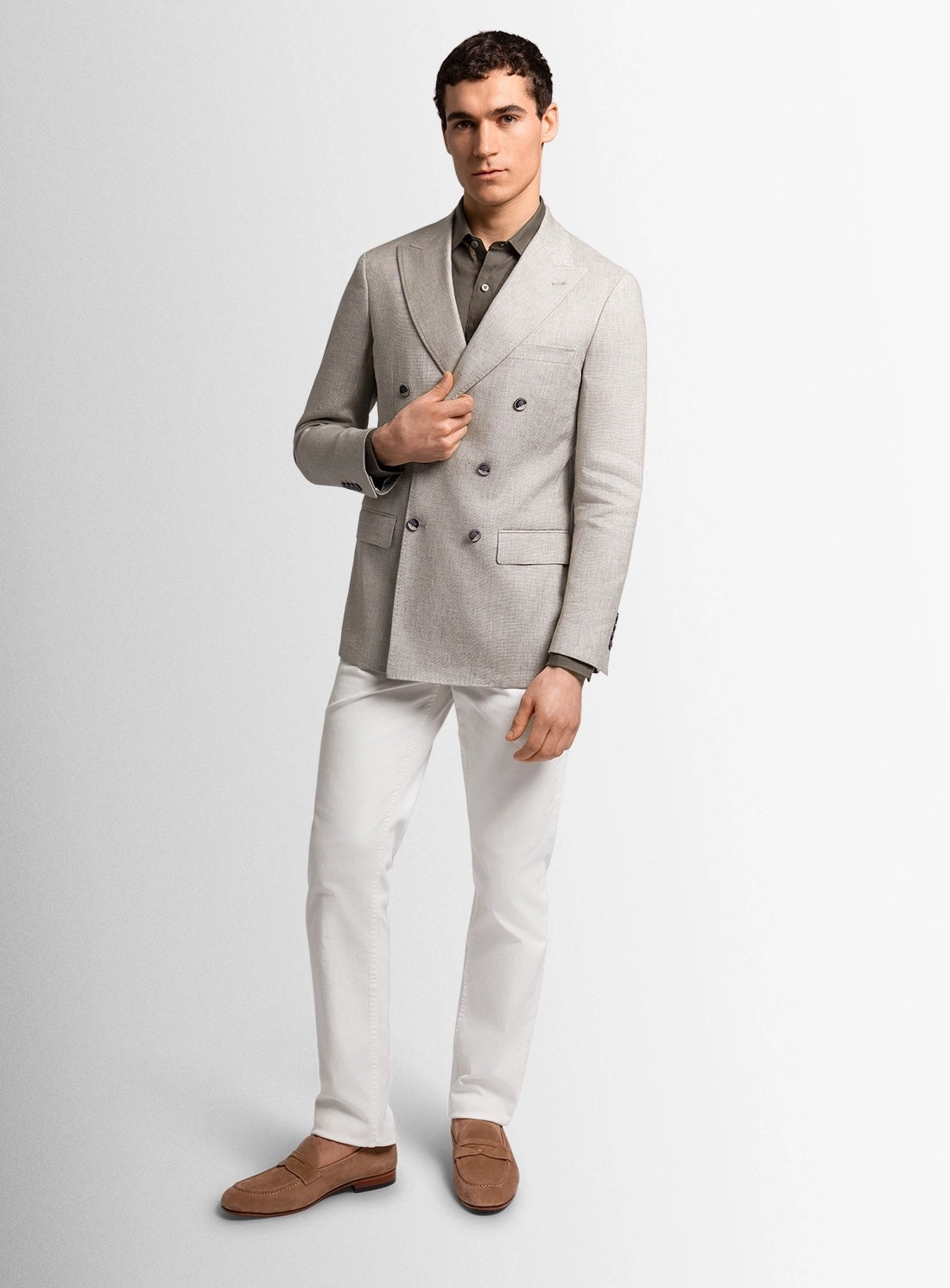 Man wearing a gray double-breasted blazer, white dress pants, and brown shoes on a light gray background