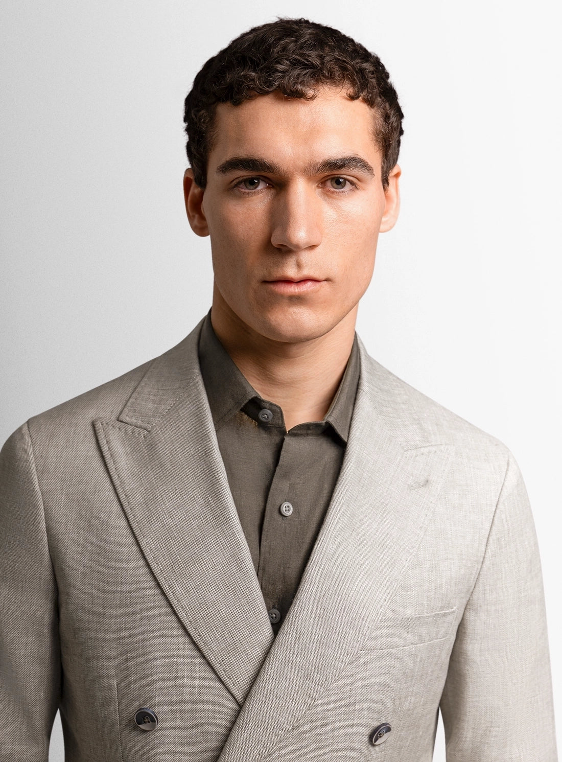 Man wearing a light gray suit jacket over a shirt on a plain background