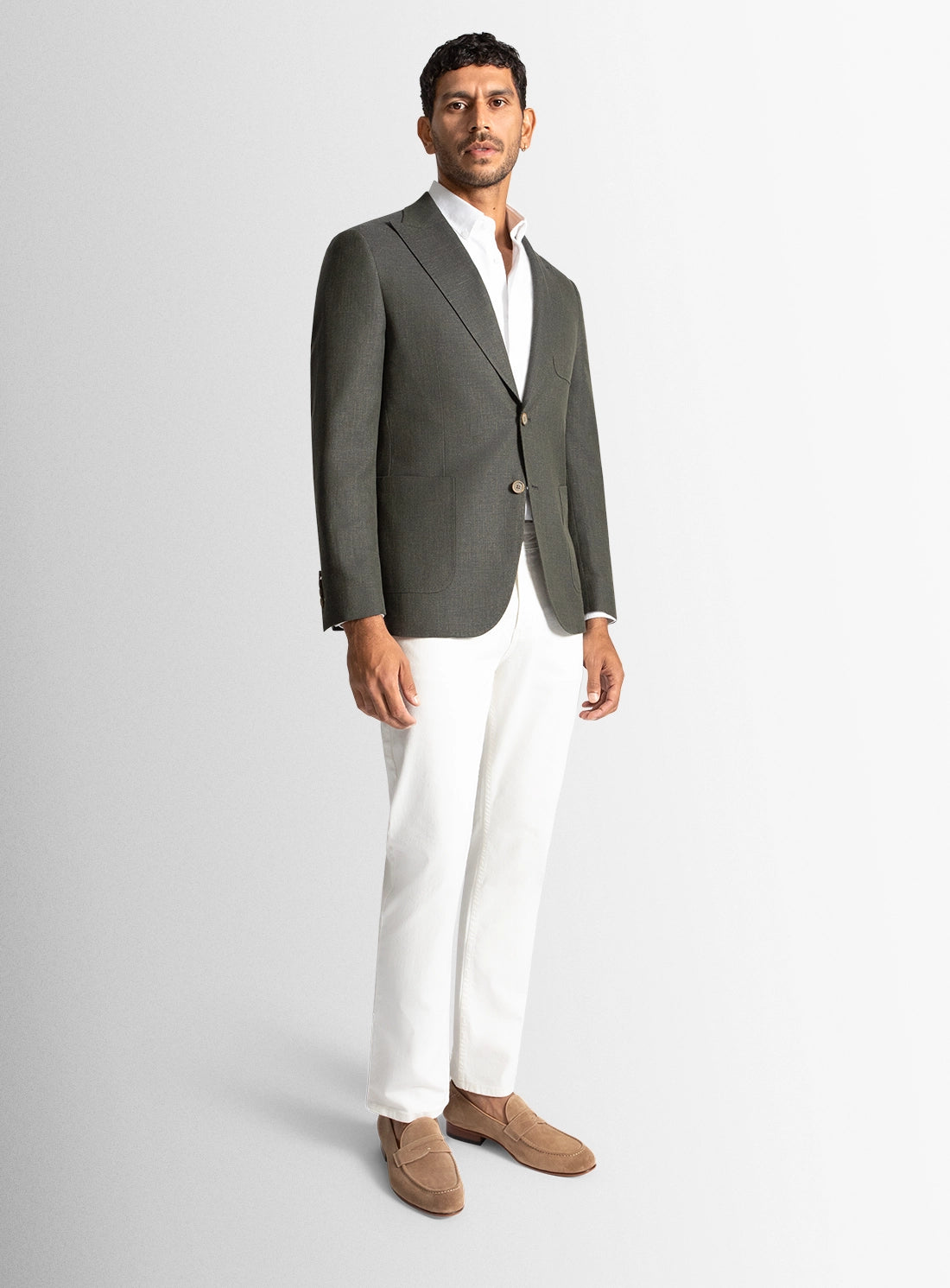 Man wearing a gray blazer, white shirt, and white pants on a light gray background