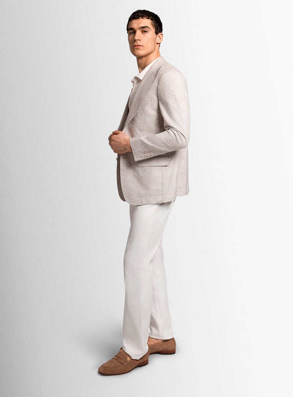 Man wearing a light gray blazer, white pants, and brown shoes on a plain background