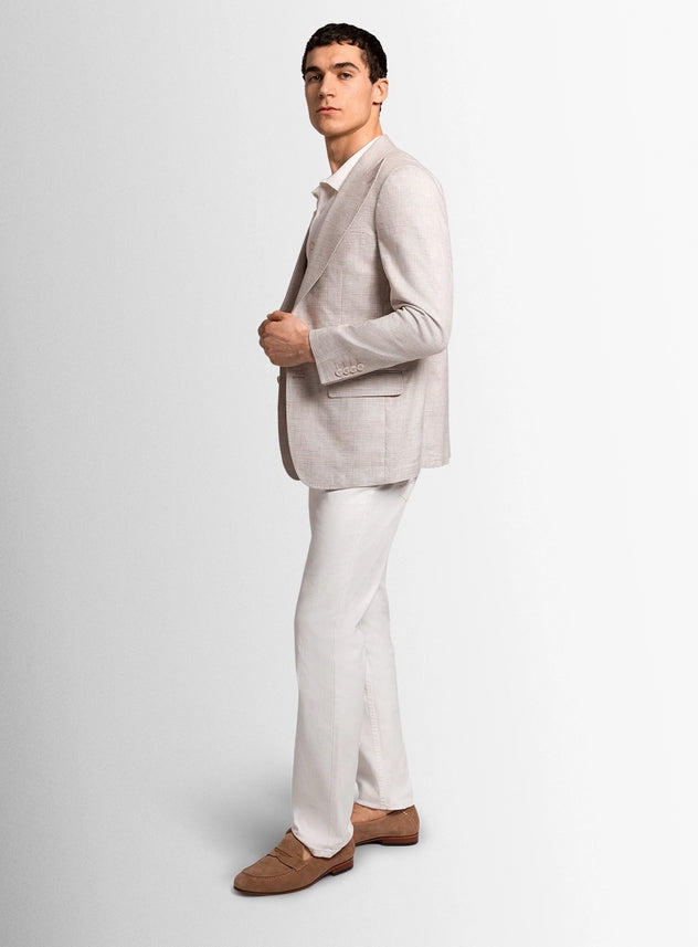 Man wearing a light gray blazer, white pants, and brown shoes on a plain background