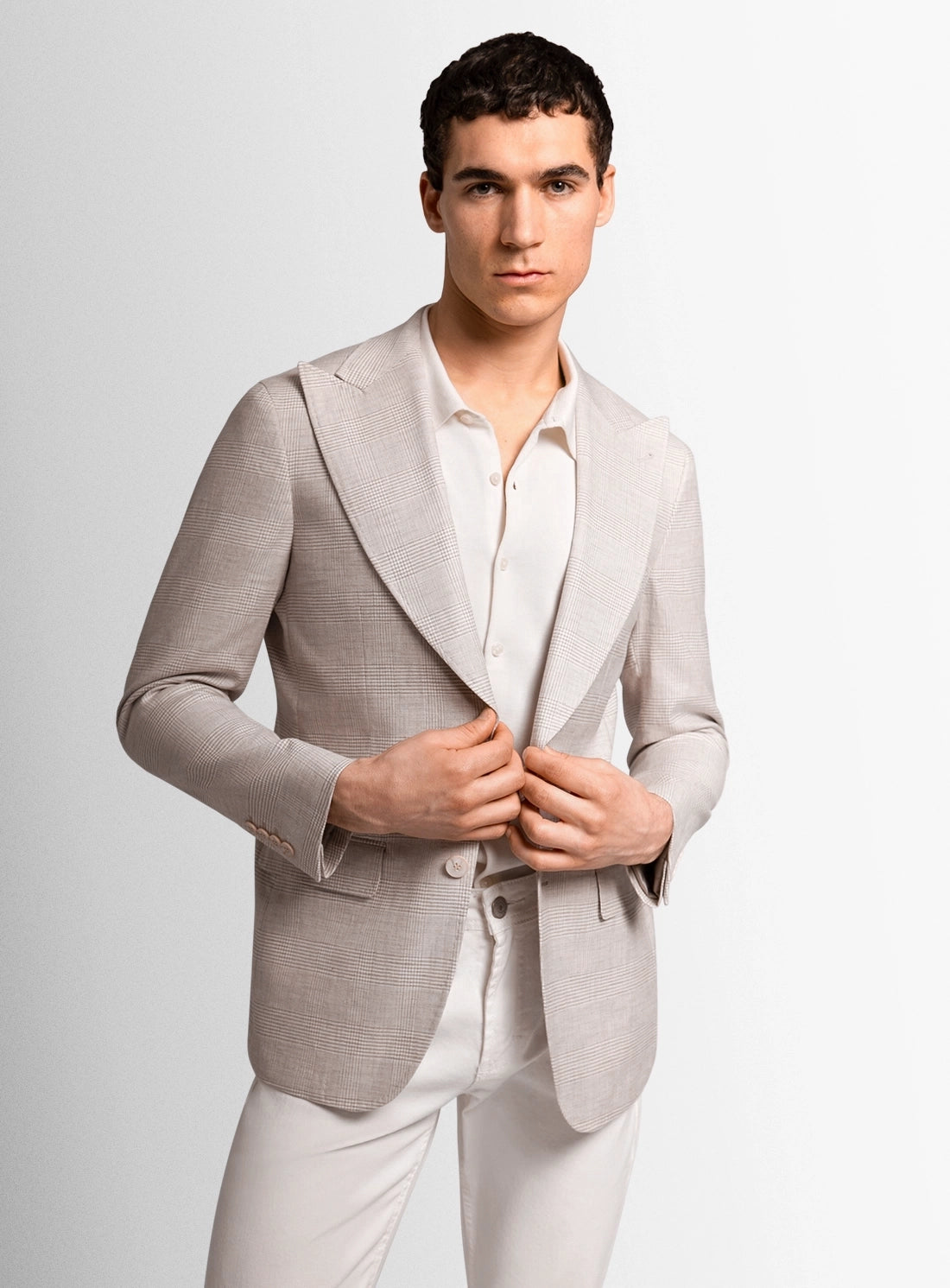 Man wearing a light gray blazer over a white shirt and pants on a plain background
