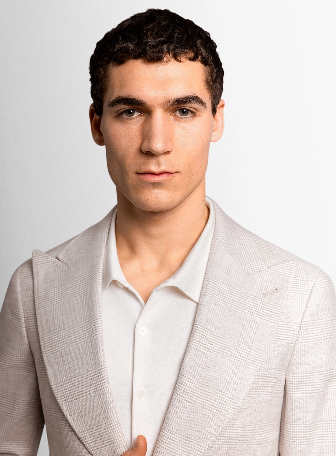 Man wearing a light gray blazer over a white shirt against a plain background