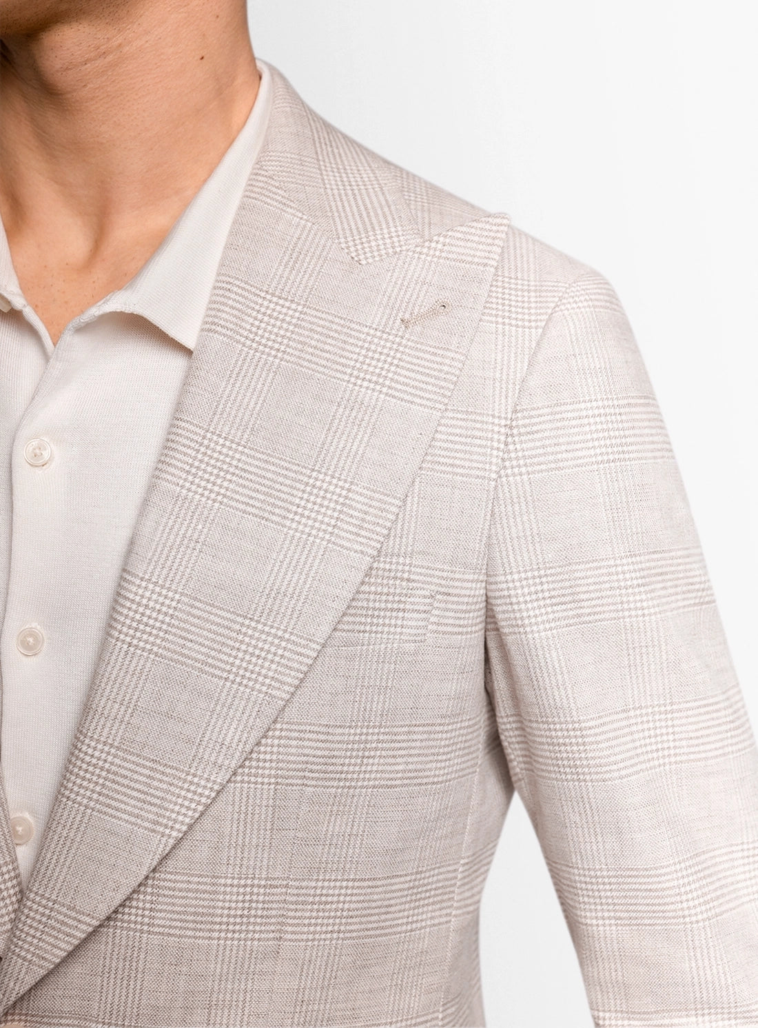 Close-up of a beige checkered blazer worn by a person on a light gray background