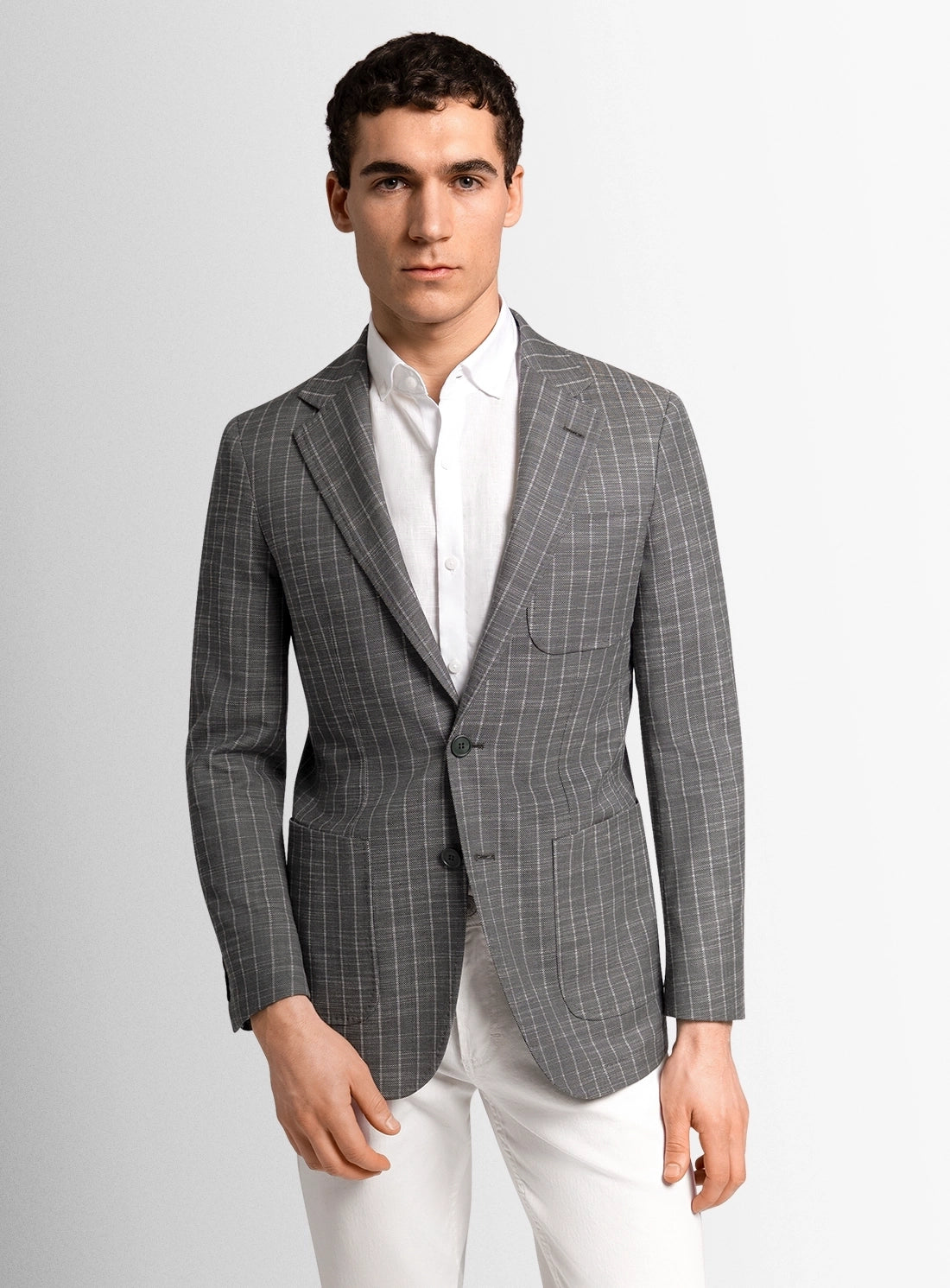 Man wearing a gray checkered blazer over a white shirt on a light gray background