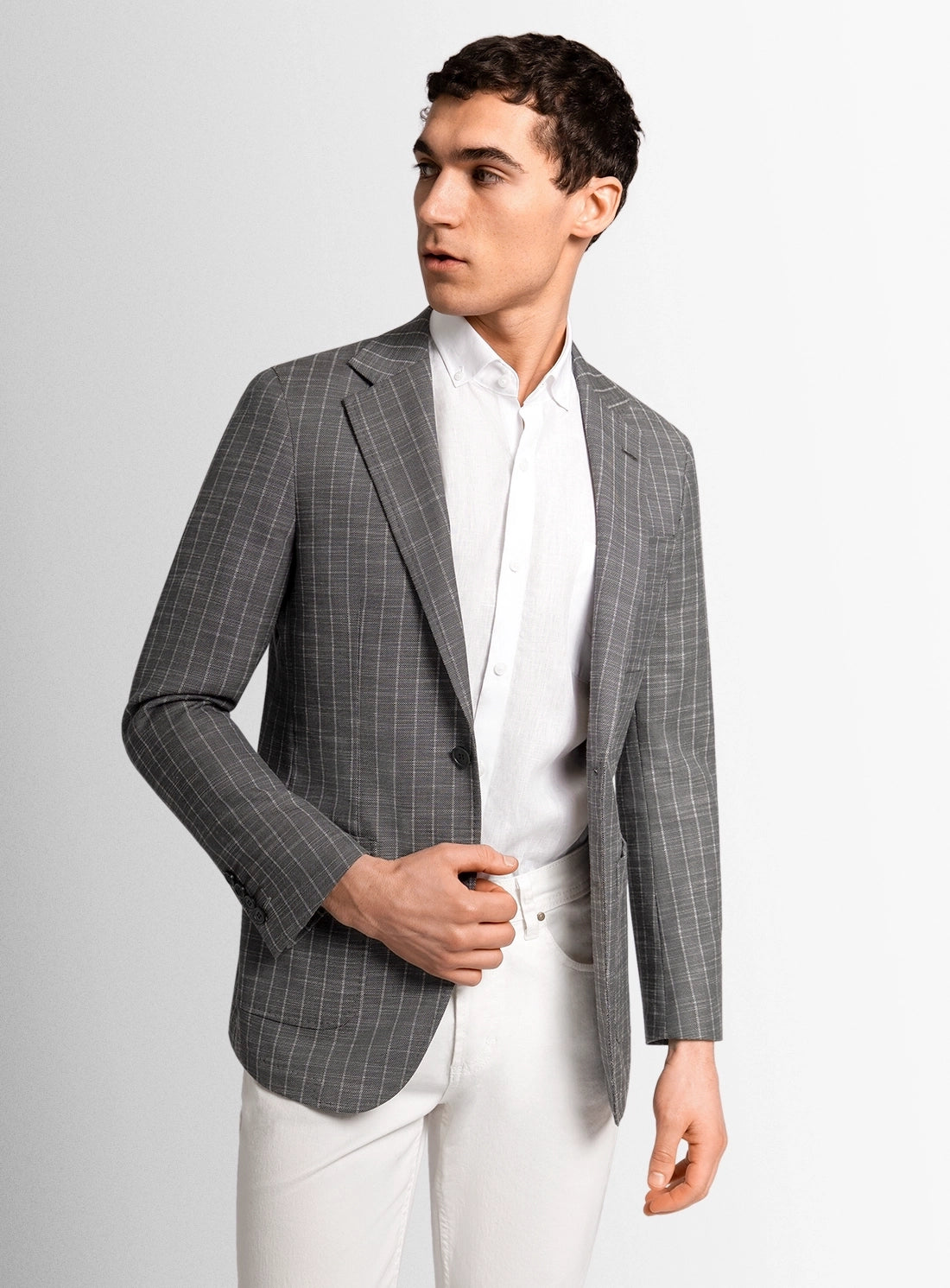 Man wearing a gray checkered blazer over a white shirt and pants on a light gray background