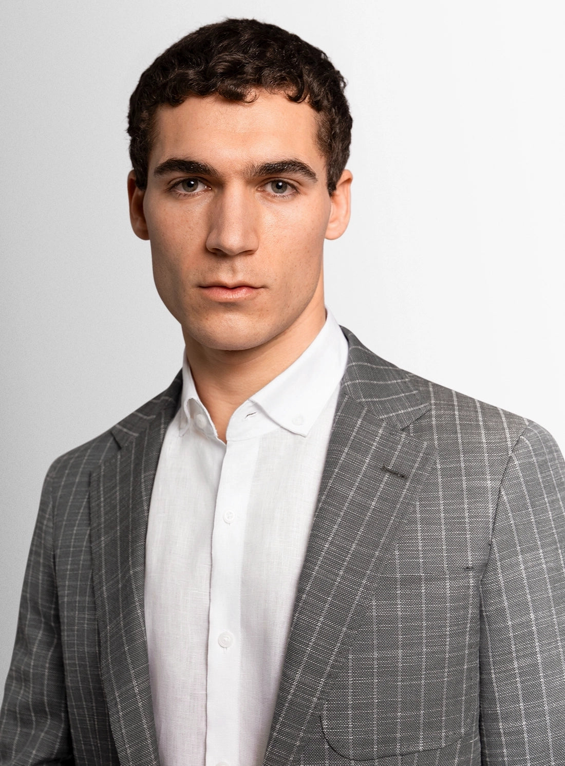 Man wearing a gray checkered suit and white shirt against a light gray background