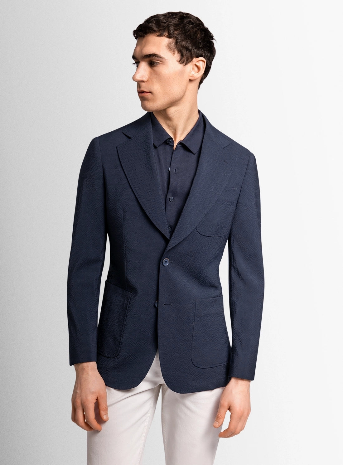 Man wearing a navy blazer over a white shirt on a light gray background