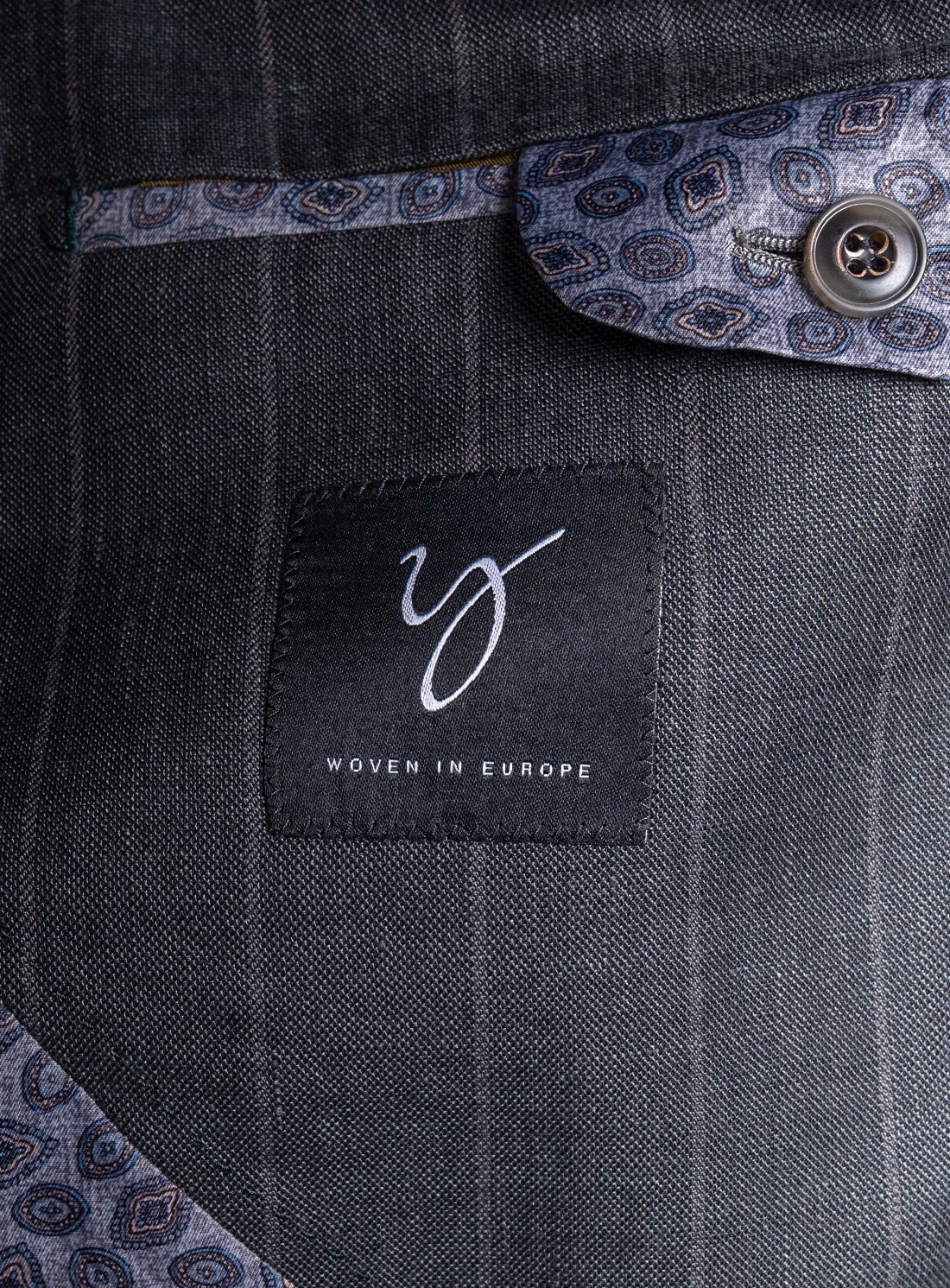 Close-up of a dark gray pinstripe suit with a brand label on the chest pocket.