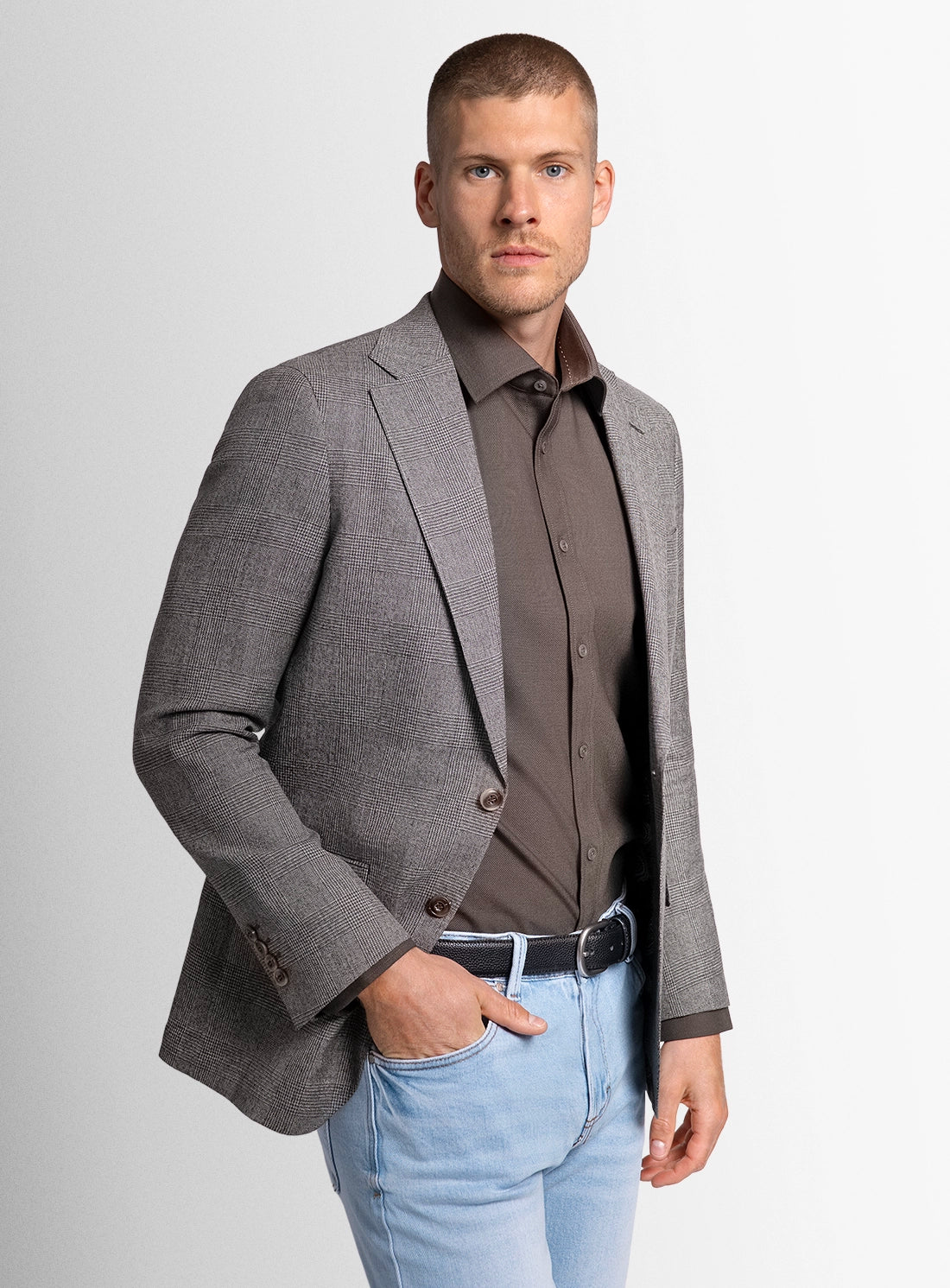 Man wearing a gray blazer over a brown shirt with light blue jeans on a white background