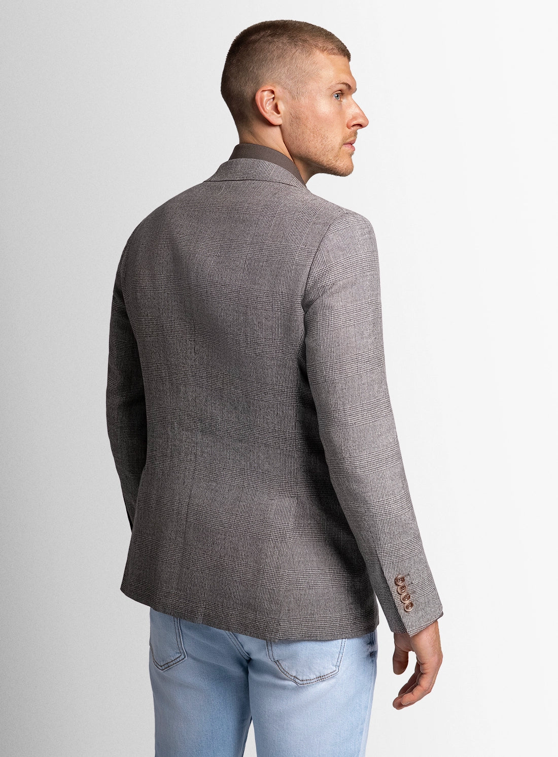 Man wearing a gray blazer and light blue jeans on a plain background