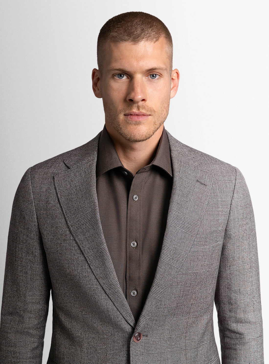 Man wearing a gray suit jacket over a brown shirt on a light gray background