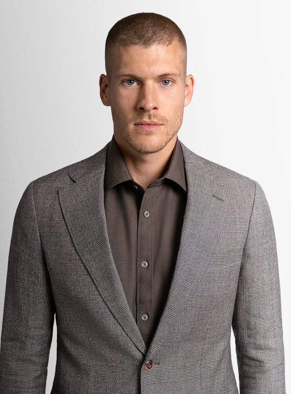 Man wearing a gray suit jacket over a brown shirt on a light gray background