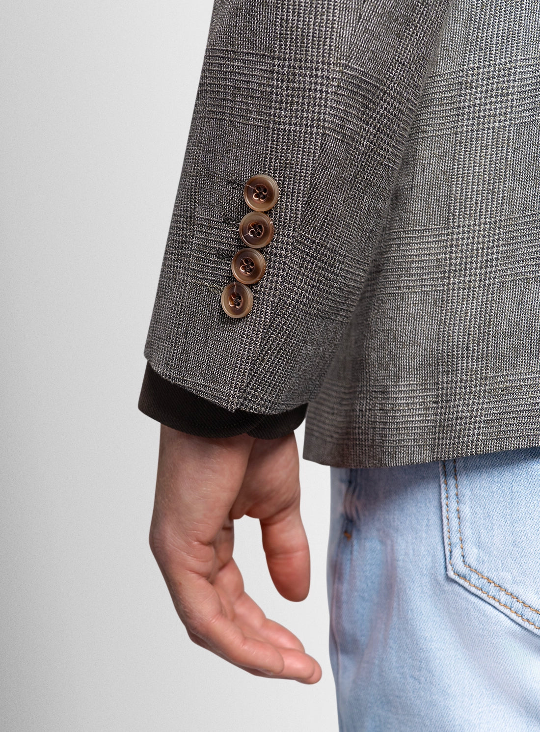 Close-up of a person wearing a gray checkered blazer with brown buttons on a light gray background