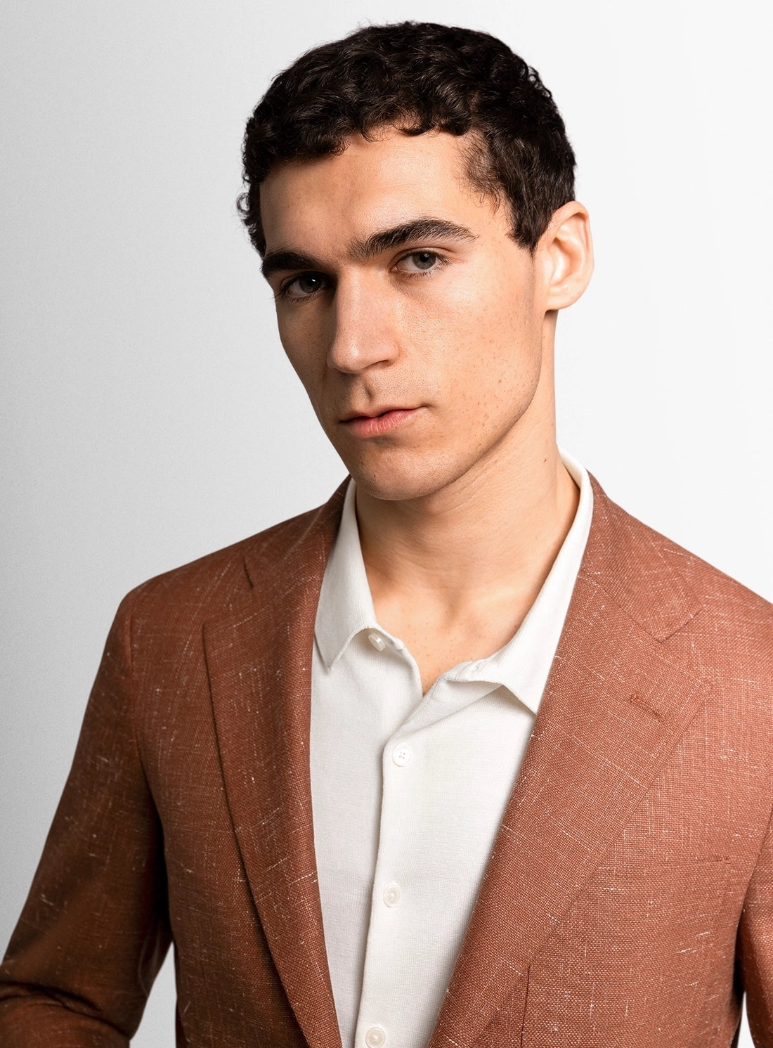 Man wearing a brown blazer over a white shirt against a plain background