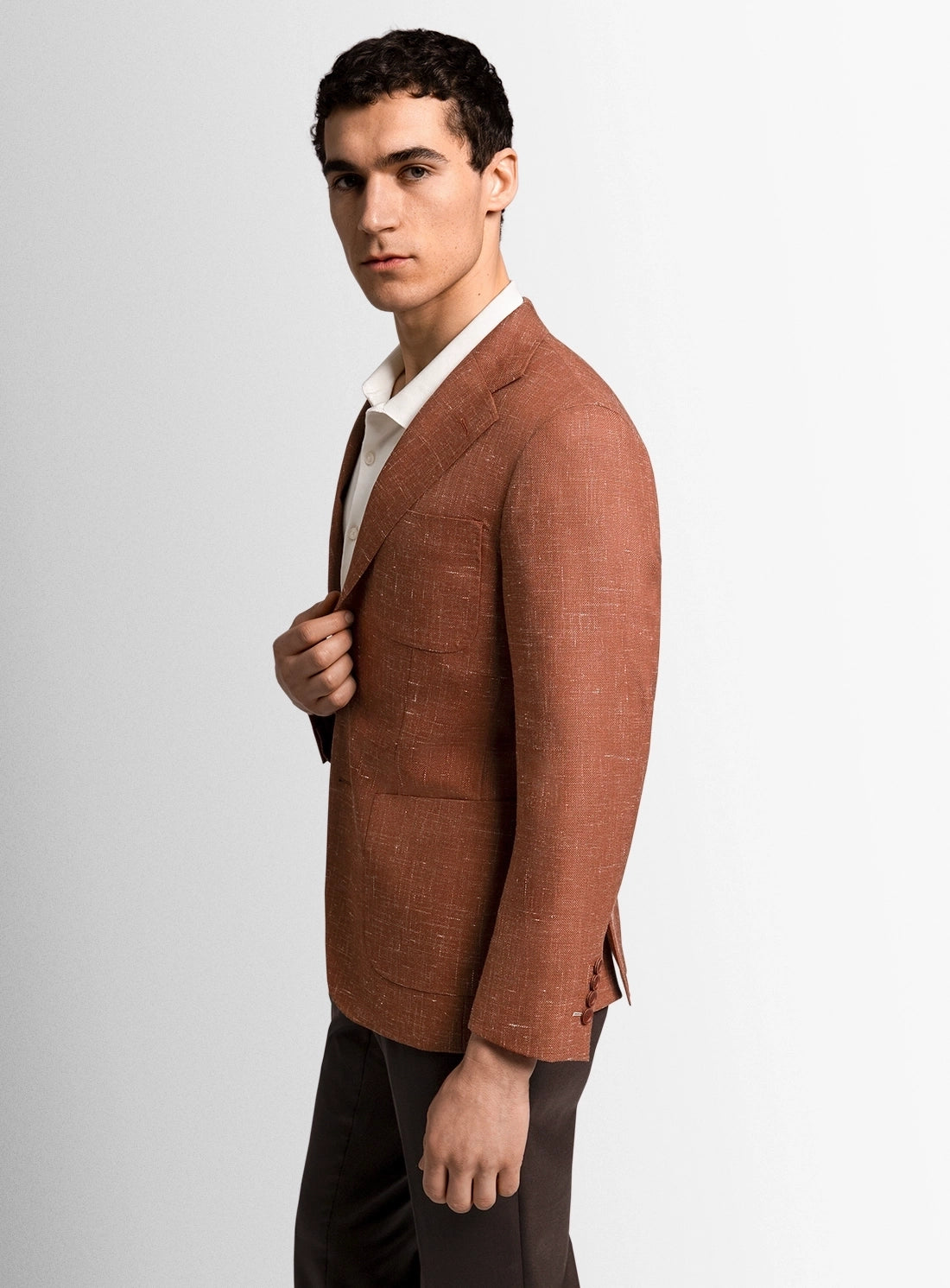 Man wearing a brown blazer over a white shirt on a light gray background