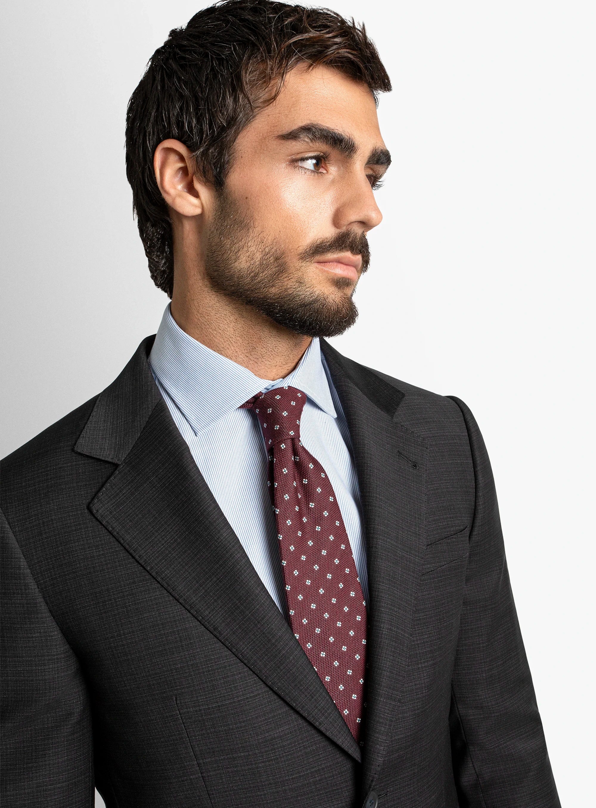 Man wearing a dark suit with a light shirt and red tie on a plain background