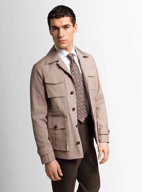 Man wearing a beige jacket and patterned tie on a plain background