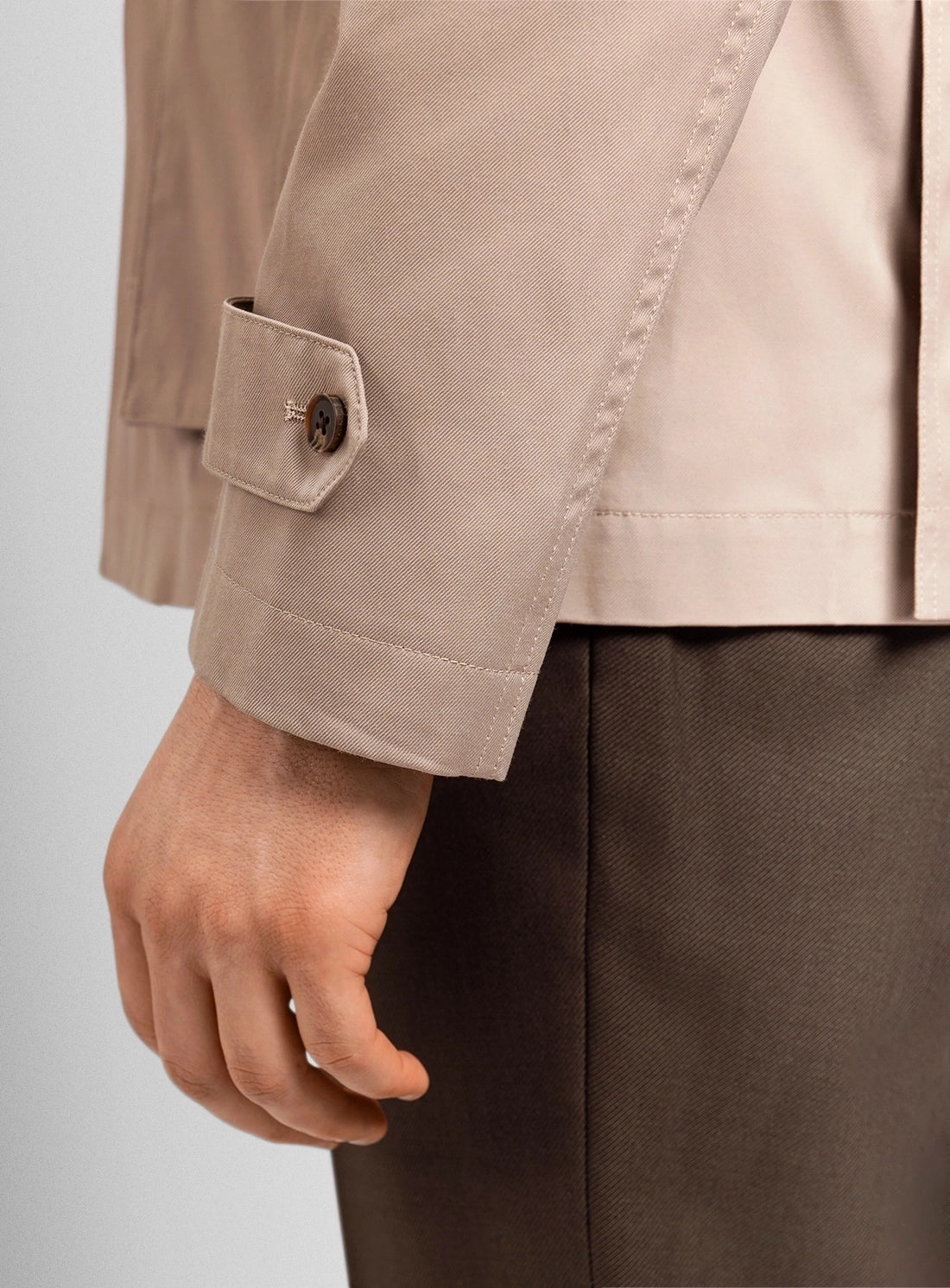 Close-up of a person wearing a beige jacket with a button on a light gray background