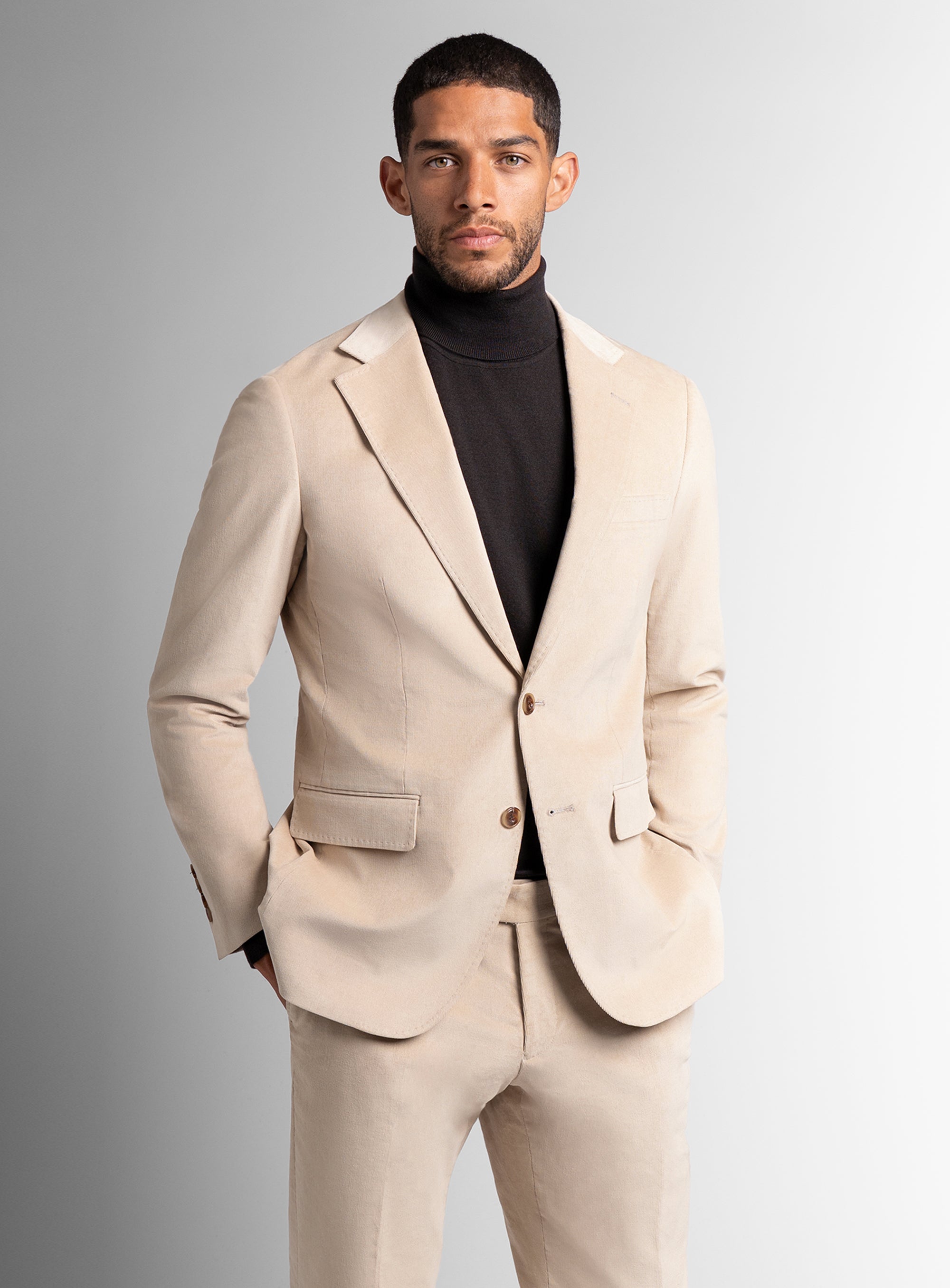 Man wearing a beige suit with a black turtleneck against a gray background