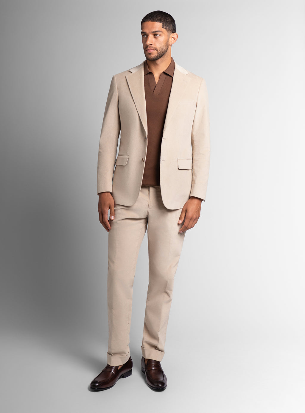 Man wearing a beige suit with a brown shirt on a gray background