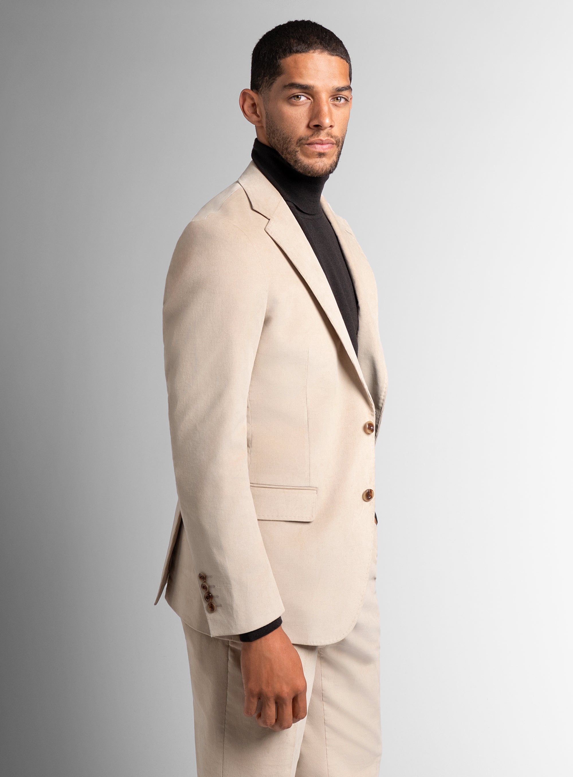 Man wearing a beige suit with a black shirt against a gray background