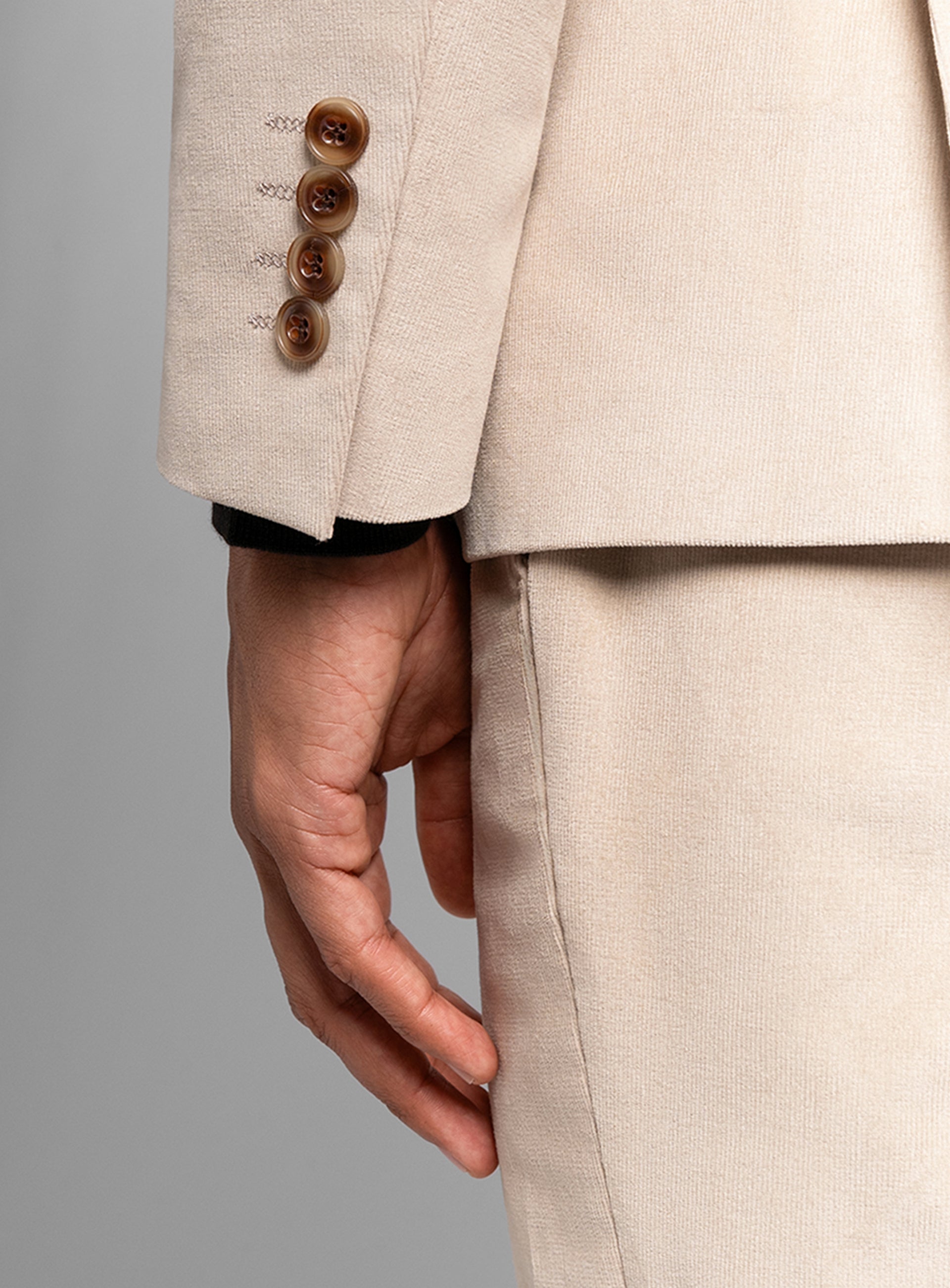 Beige suit jacket with three buttons and matching pants on a gray background